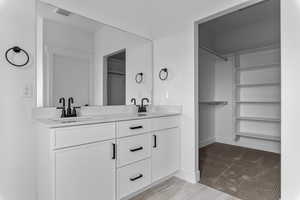 Bathroom featuring a spacious closet, double vanity, and light carpet
