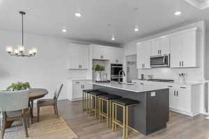 Kitchen featuring a kitchen island with sink, a breakfast bar, dark wood finished floors, two tone color scheme, and light stone counters