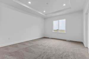 Empty room featuring recessed lighting, light carpet, and a tray ceiling