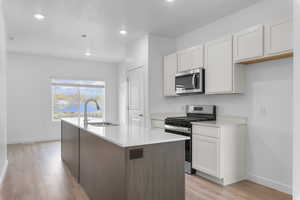Two tone kitchen with stainless steel appliances, light wood-style flooring, an island with sink, recessed lighting, and light stone countertops