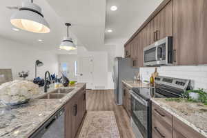 Kitchen with stainless steel appliances, light stone countertops, decorative light fixtures, and a textured ceiling