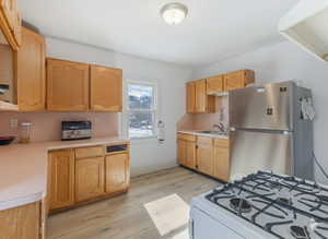 Kitchen featuring freestanding refrigerator, white range with gas cooktop, light countertops, light wood-type flooring, and light wood finish cabinets