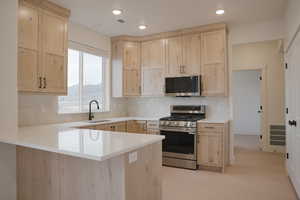 Kitchen with light wood finish cabinetry, stainless steel appliances, a peninsula, backsplash, and light wood-type flooring