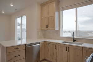 Kitchen featuring light wood finish cabinetry, stainless steel dishwasher, decorative backsplash, light stone counters, and a peninsula