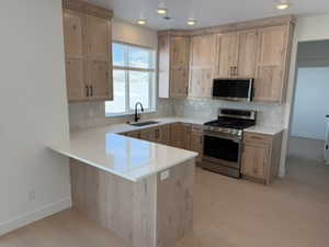 Kitchen featuring light wood finish cabinetry, stainless steel appliances, a peninsula, and light wood-style floors