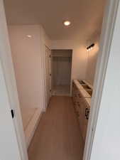 Full bathroom with a walk in closet, vanity, light wood finished floors, and a shower
