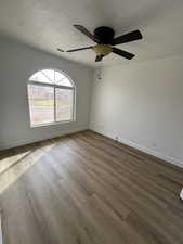 Empty room with ceiling fan, wood finished floors, and a textured ceiling