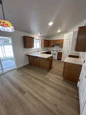 Kitchen with light countertops, a peninsula, white range oven, wood finish cabinets, and decorative light fixtures