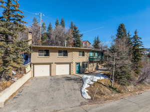 View of front of home with a chimney, an attached garage, driveway, brick siding, and a balcony