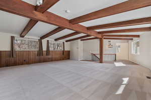 Unfurnished living room featuring light carpet, beamed ceiling, and wood walls