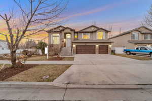 View of front facade with driveway, an attached garage, stucco siding, and stone siding