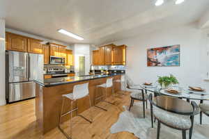 Kitchen featuring wood finish cabinetry, a peninsula, stainless steel appliances, a breakfast bar area, and dark stone counters