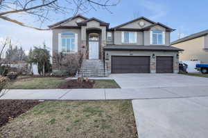 View of front of house featuring stucco siding, driveway, stone siding, an attached garage, and a front yard