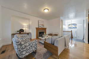 Living room with hardwood / wood-style floors, a tiled fireplace, suspended lighting, a textured ceiling, and arched walkways