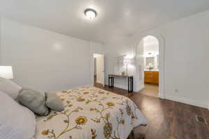 Bedroom featuring dark wood-type flooring, arched walkways, and ensuite bathroom