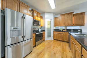 Kitchen with stainless steel appliances, dark stone countertops, light wood-type flooring, wood finish cabinets, and decorative backsplash