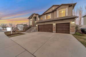 View of front of house with stone siding, an attached garage, concrete driveway, and stucco siding