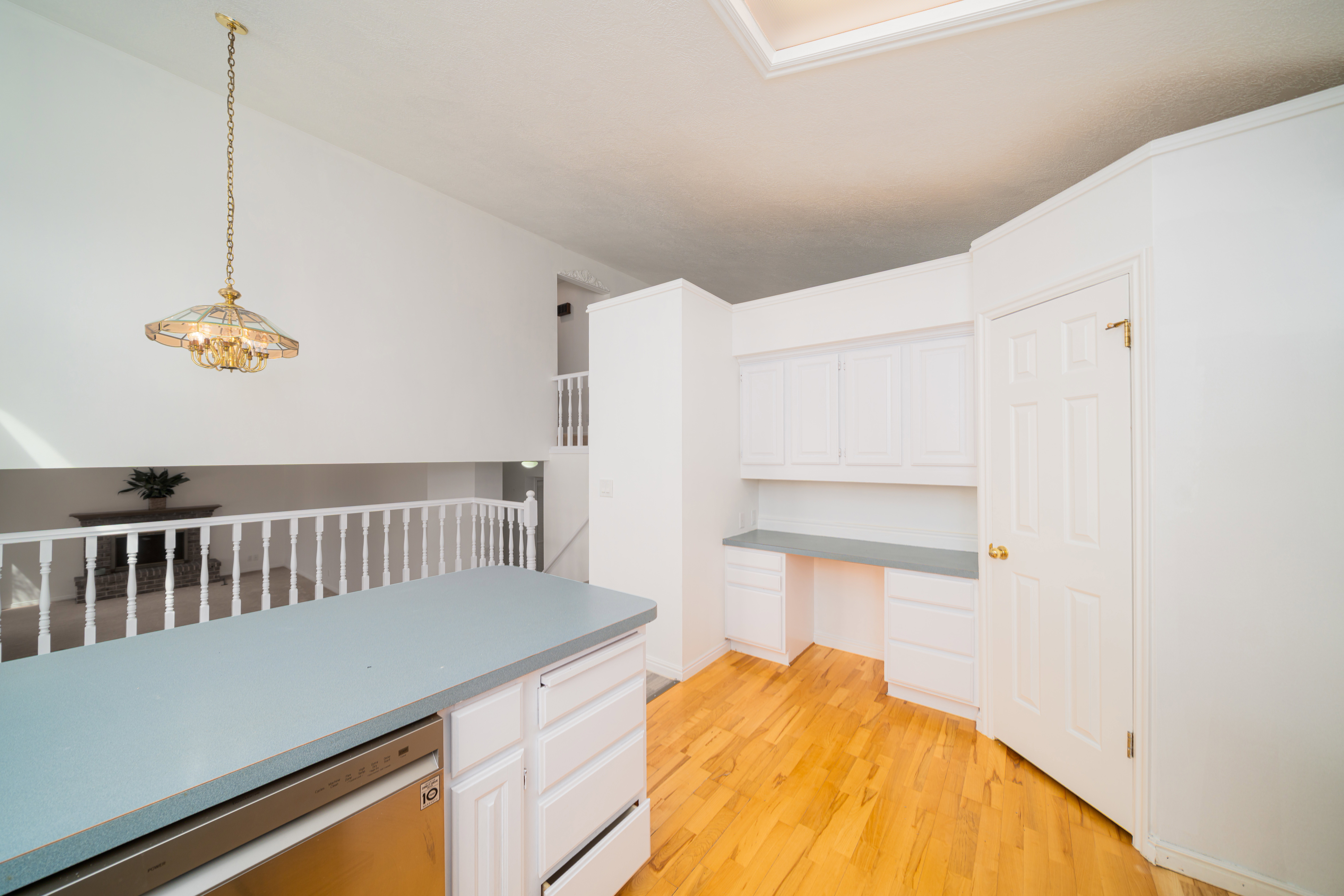 Kitchen with stainless steel dishwasher, hanging light fixtures, light wood-style floors, built in desk, and white cabinets