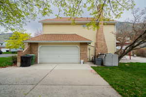 View of side of home with driveway, a yard, brick siding, and an attached garage