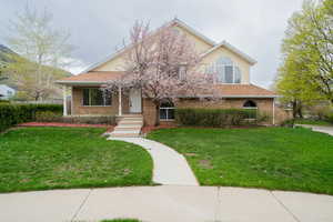 View of front of house with covered porch, a front lawn, brick siding, and roof with shingles