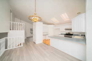 Kitchen featuring suspended lighting, a peninsula, white cabinetry, gas stove, and light countertops