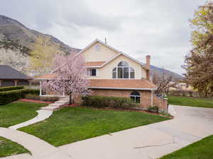 View of front facade featuring a mountain view, brick siding, a front yard, roof with shingles, and a chimney