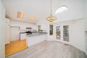 Kitchen featuring a peninsula, white cabinets, a chandelier, stainless steel range with gas cooktop, and light wood-type flooring