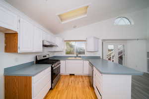 Kitchen featuring stainless steel appliances, light wood-style floors, a peninsula, vaulted ceiling, and white cabinetry