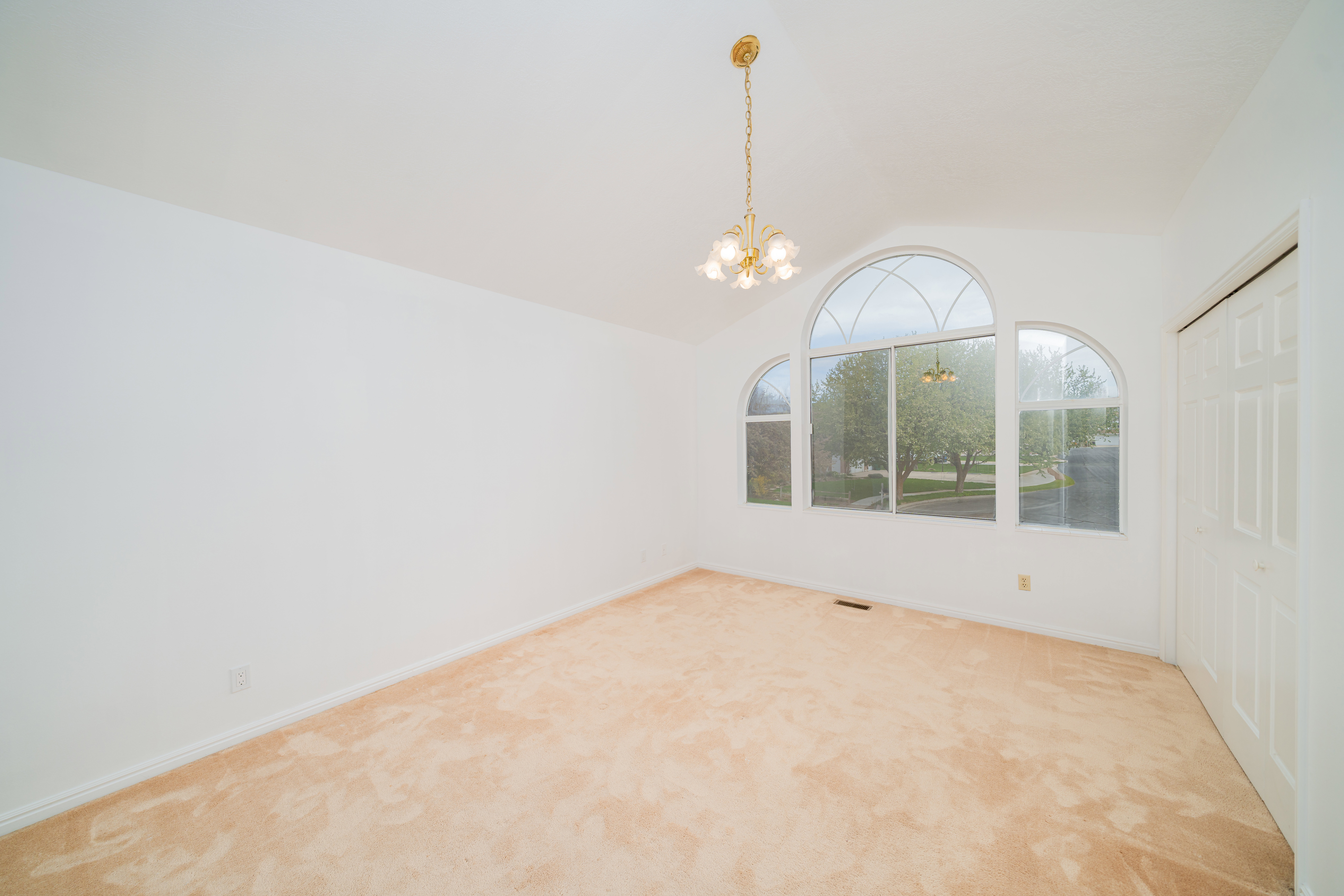 Carpeted spare room with hanging lights and vaulted ceiling