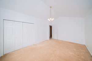 Unfurnished bedroom featuring hanging lights, carpet floors, lofted ceiling, and a closet