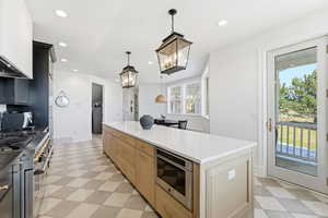Kitchen featuring stainless steel appliances, two tone cabinetry, a large island with sink, light floors, and dark stone counters
