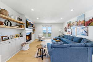 Living room with a warm lit fireplace, light wood-type flooring, and recessed lighting