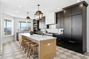 Kitchen with two tone cabinetry, a breakfast bar, a kitchen island with sink, light flooring, and dark stone countertops