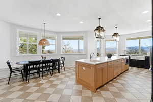 Dual tone kitchen with decorative light fixtures, an island with sink, light stone counters, and two tone color scheme