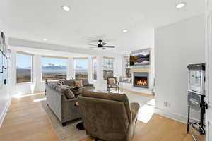 Living room featuring a lit fireplace, light wood finished floors, recessed lighting, and a ceiling fan