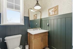 Half bathroom with a wainscoted wall, vanity, and wallpapered walls