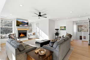 Living room featuring a lit fireplace, light wood-type flooring, a ceiling fan, plenty of natural light, and recessed lighting