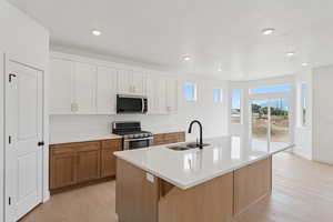 Two tone kitchen featuring stainless steel appliances, light wood finished floors, a center island with sink, dual tone cabinets, and light stone countertops