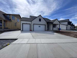 View of front facade with stucco siding, an attached garage, driveway, and roof with shingles