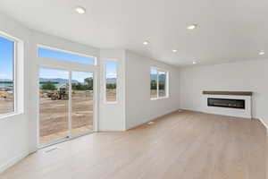 Unfurnished living room featuring light wood-style flooring, a glass covered fireplace, a mountain view, and recessed lighting