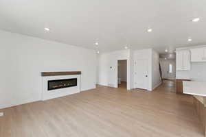 Unfurnished living room featuring light wood-style flooring, a glass covered fireplace, and recessed lighting