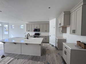 Kitchen with gray cabinetry, light stone counters, electric range, a breakfast bar area, and an island with sink