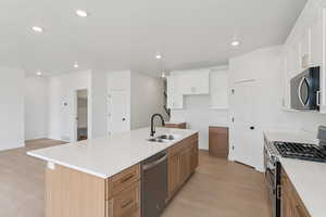 Kitchen featuring stainless steel appliances, dual tone cabinets, light wood-style flooring, a kitchen island with sink, and light stone countertops