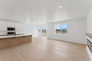 Dual tone kitchen with a breakfast bar area, light wood-style flooring, stainless steel appliances, open floor plan, and two tone cabinetry