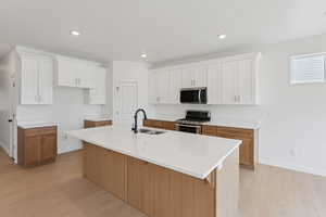 Kitchen featuring two tone cabinetry, stainless steel appliances, light wood-style floors, a center island with sink, and a kitchen bar
