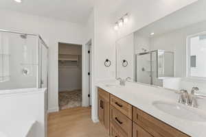 Bathroom featuring a stall shower, a walk in closet, double vanity, a bath, and light wood-style floors