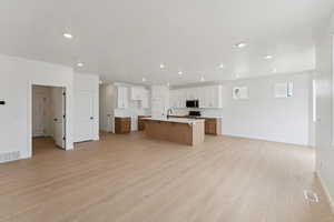 Dual tone kitchen featuring open floor plan, a kitchen island with sink, a breakfast bar, light wood finished floors, and light countertops