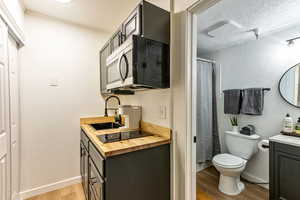 Full bathroom featuring a textured wall, vanity, light wood-type flooring, a shower with curtain, and a textured ceiling
