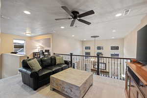 Living area with light colored carpet, a textured ceiling, a desk, hanging lights, and ceiling fan