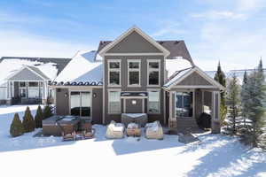 Snow covered property featuring a hot tub, a patio, stucco siding, and stone siding